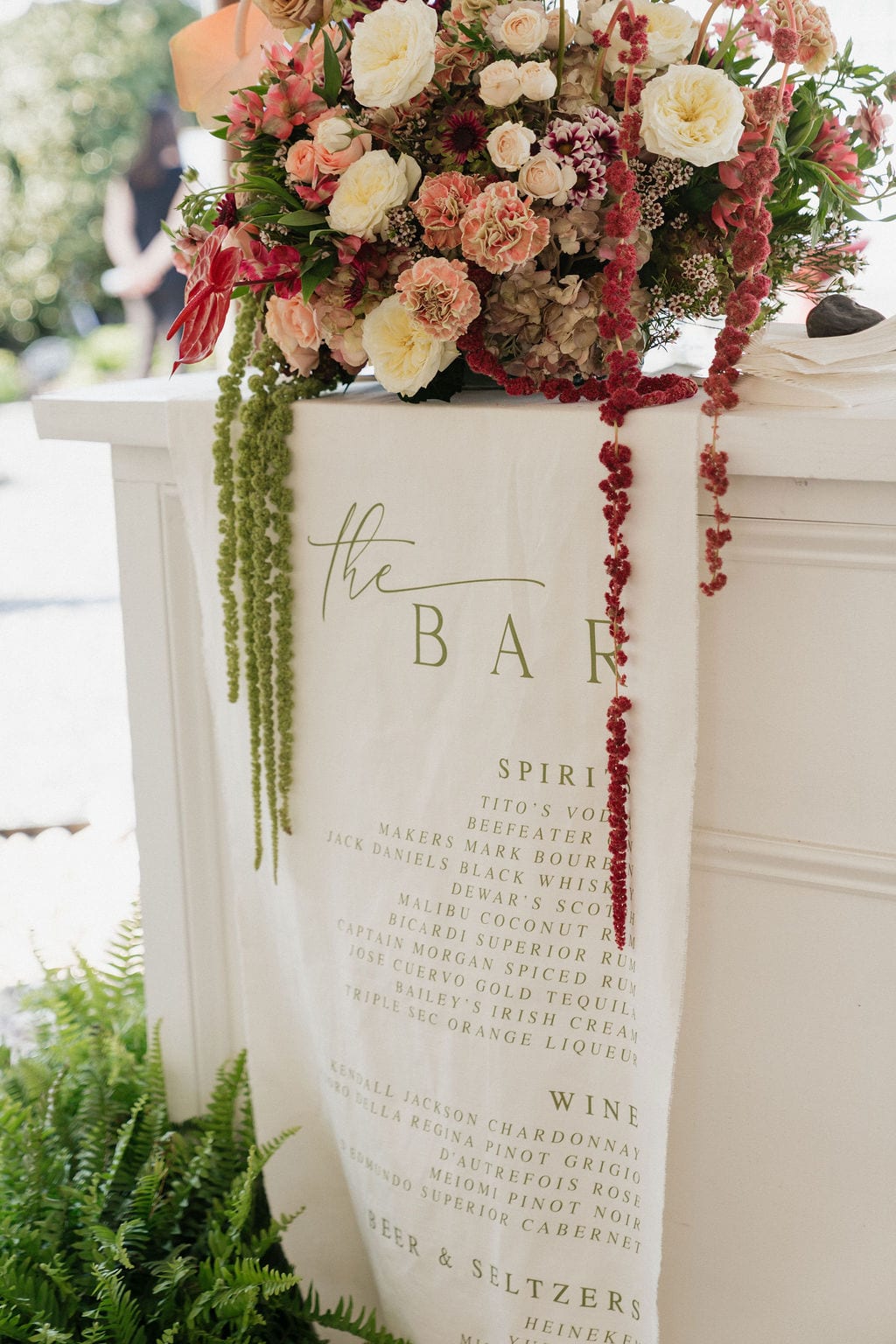 Bar-top arrangement with trailing amaranthus over a linen bar menu at the Callie & Jeremy wedding — designed by Lael Florals