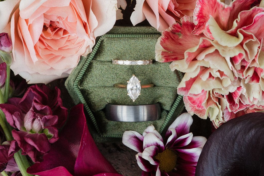 Wedding rings in a green velvet box surrounded by roses and carnations at the Callie & Jeremy wedding — designed by Lael Florals