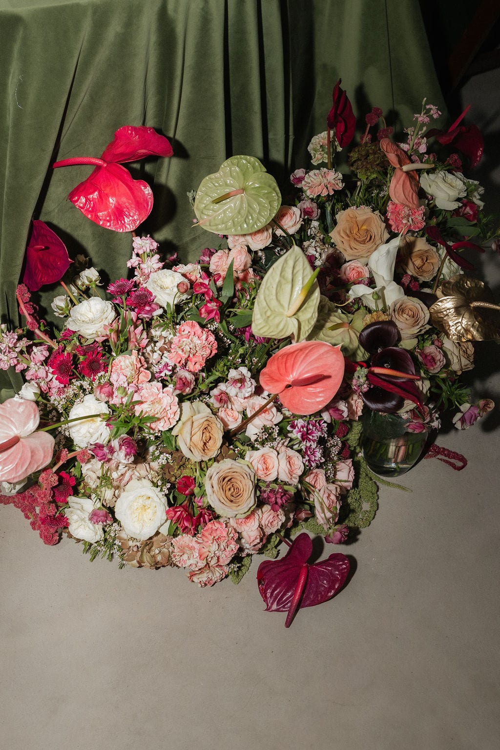 Pink anthurium, rose, and carnation floral installation on green velvet at the Callie & Jeremy wedding — designed by Lael Florals