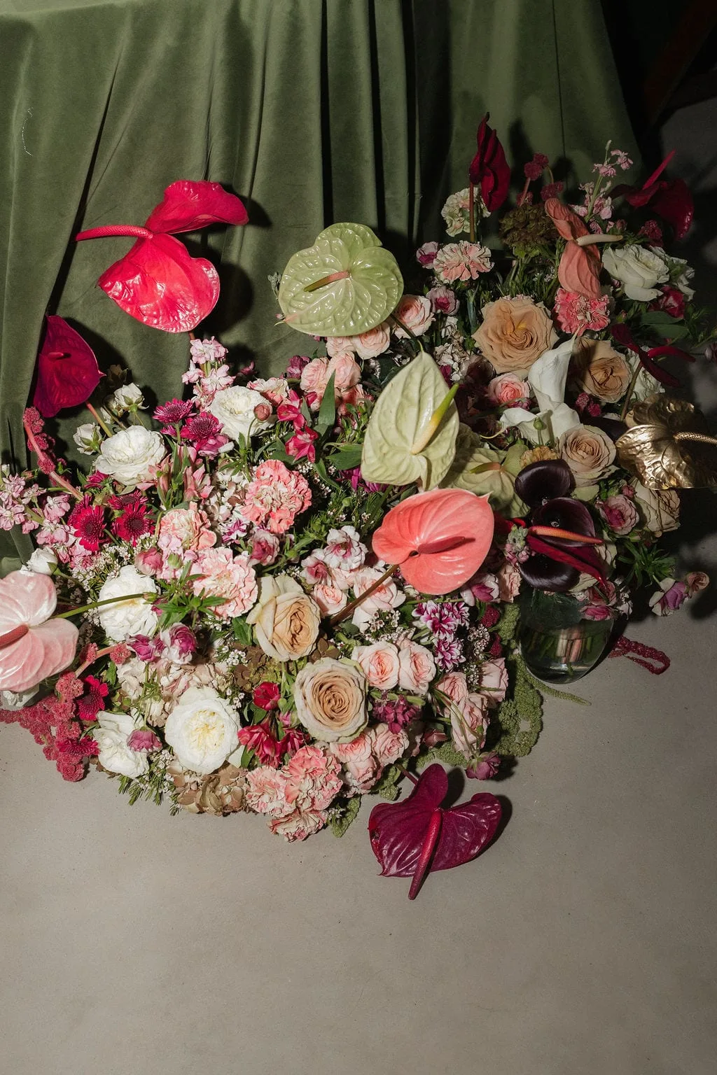 Overhead of garden roses and anthurium massed on olive velvet