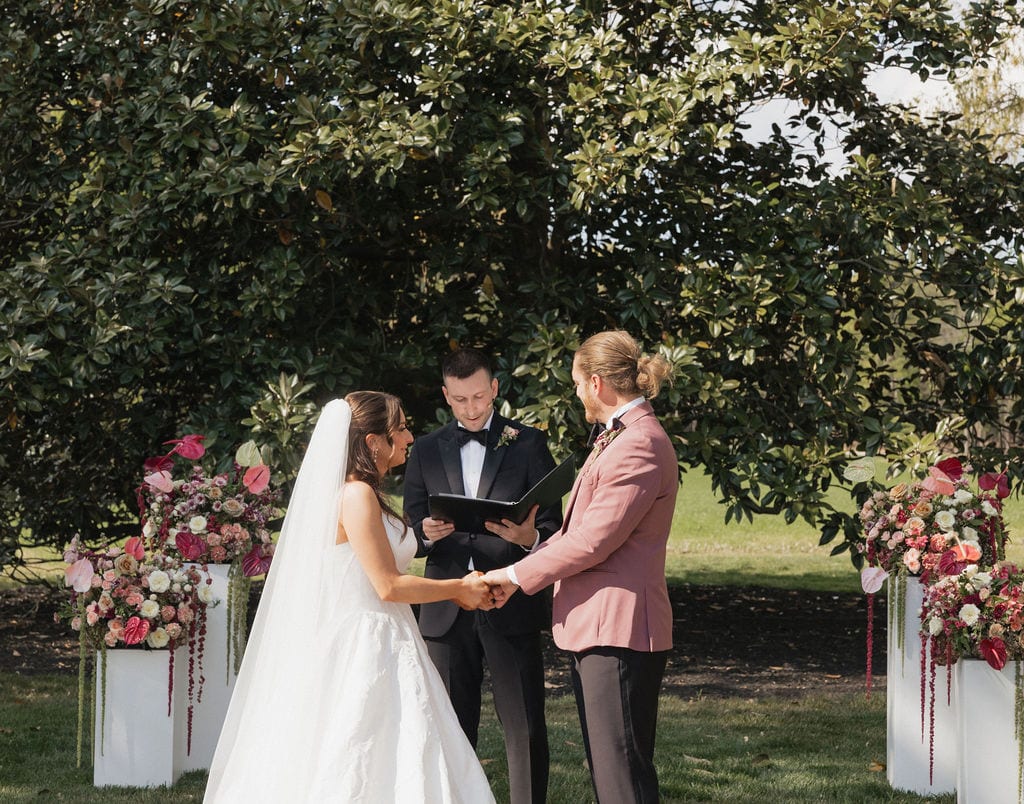 Couple exchanging vows between pink anthurium pillar arrangements at the Callie & Jeremy wedding — designed by Lael Florals