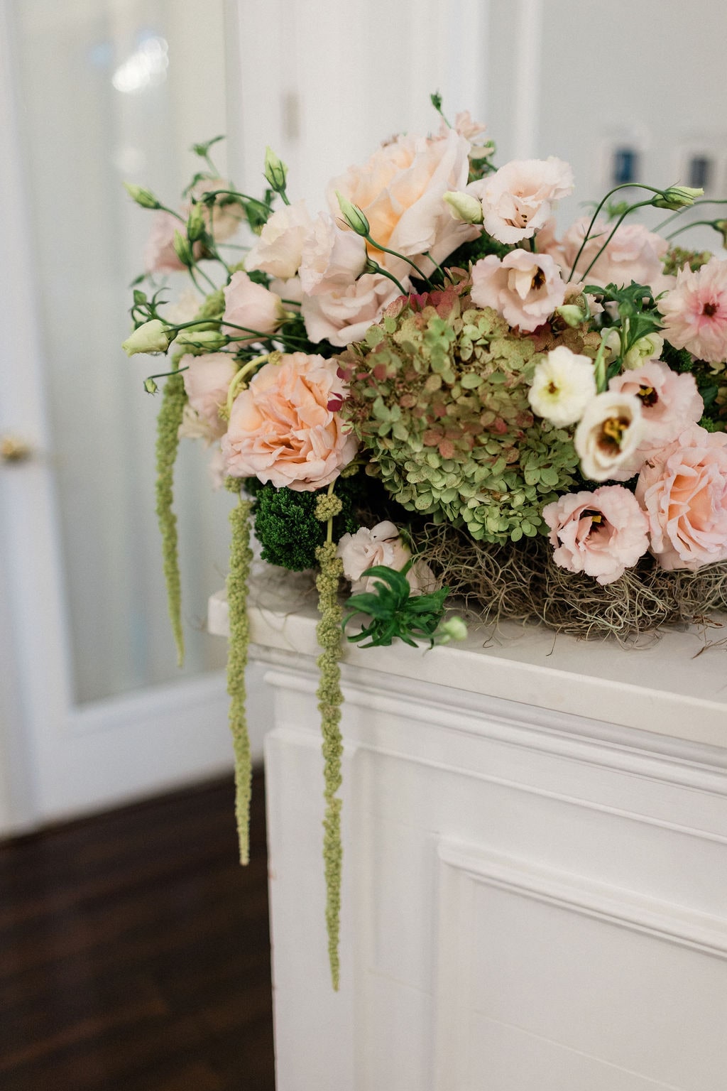 Blush roses, lisianthus, green hydrangea and hanging amaranthus up close against a white ground at the Emily & Thomas wedding — designed by Lael Florals