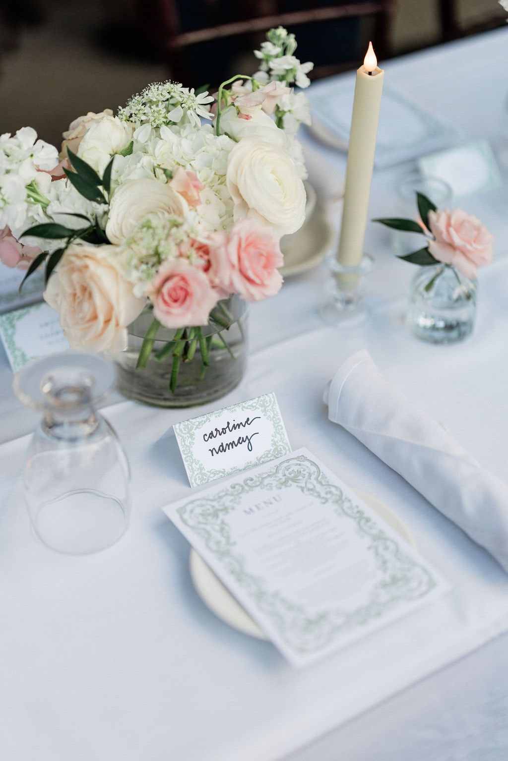 Blush and cream roses with white blooms and a taper over the place setting at the Emily & Thomas wedding — designed by Lael Florals