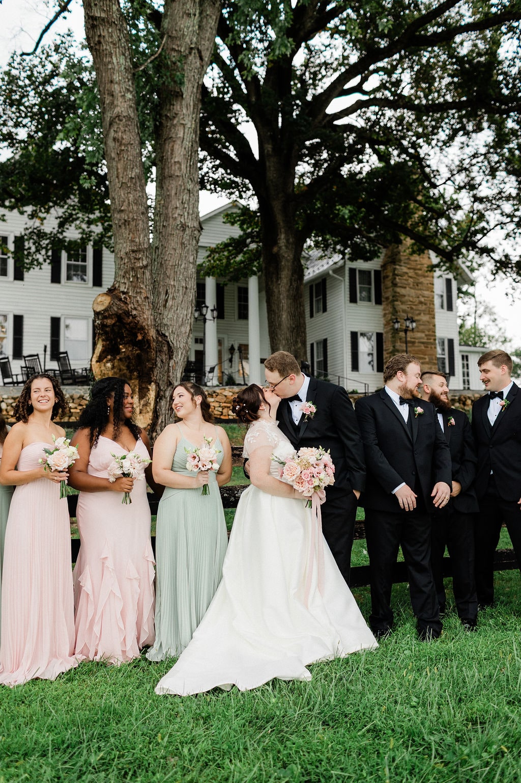 The bride and bridesmaids on the lawn, blush and ivory bouquets held forward against sage and pink gowns, at the Emily & Thomas wedding — designed by Lael Florals