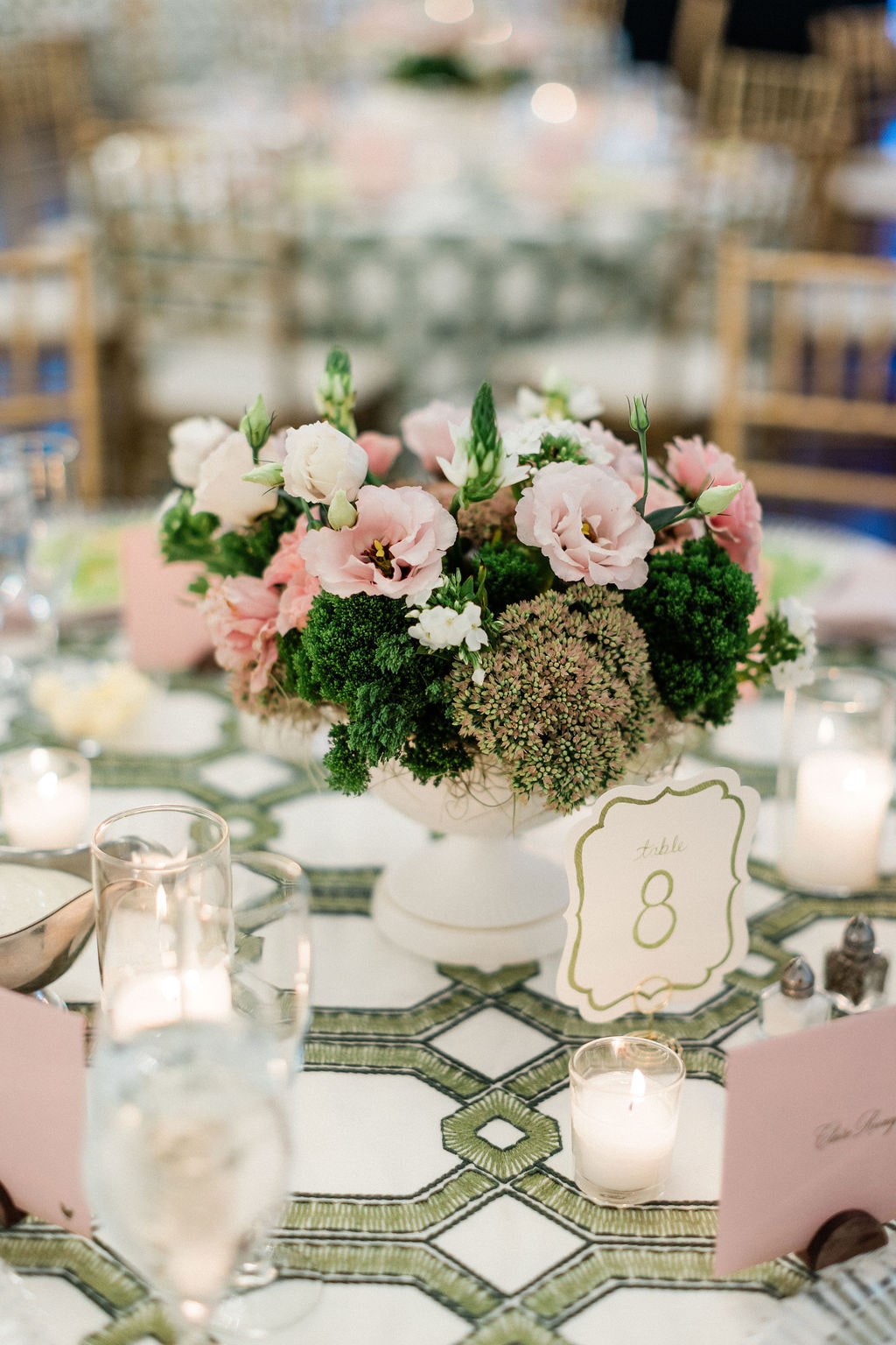 Pink lisianthus, green hydrangea and roses in a white footed vessel with the table number in candlelight at the Emily & Thomas wedding — designed by Lael Florals