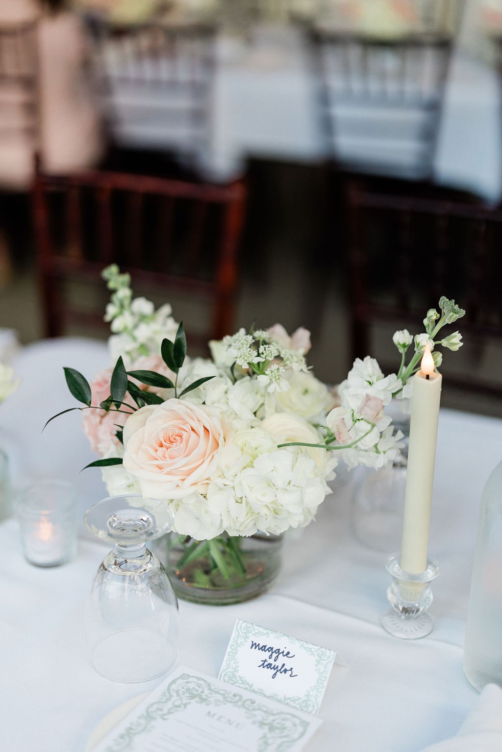 A white hydrangea and blush rose centerpiece among candles, chiavari chairs soft behind, at the Emily & Thomas wedding — designed by Lael Florals