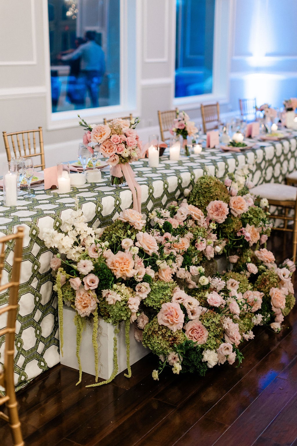 The head table runner of blush roses and hydrangea spilling over the front edge in window light at the Emily & Thomas wedding — designed by Lael Florals