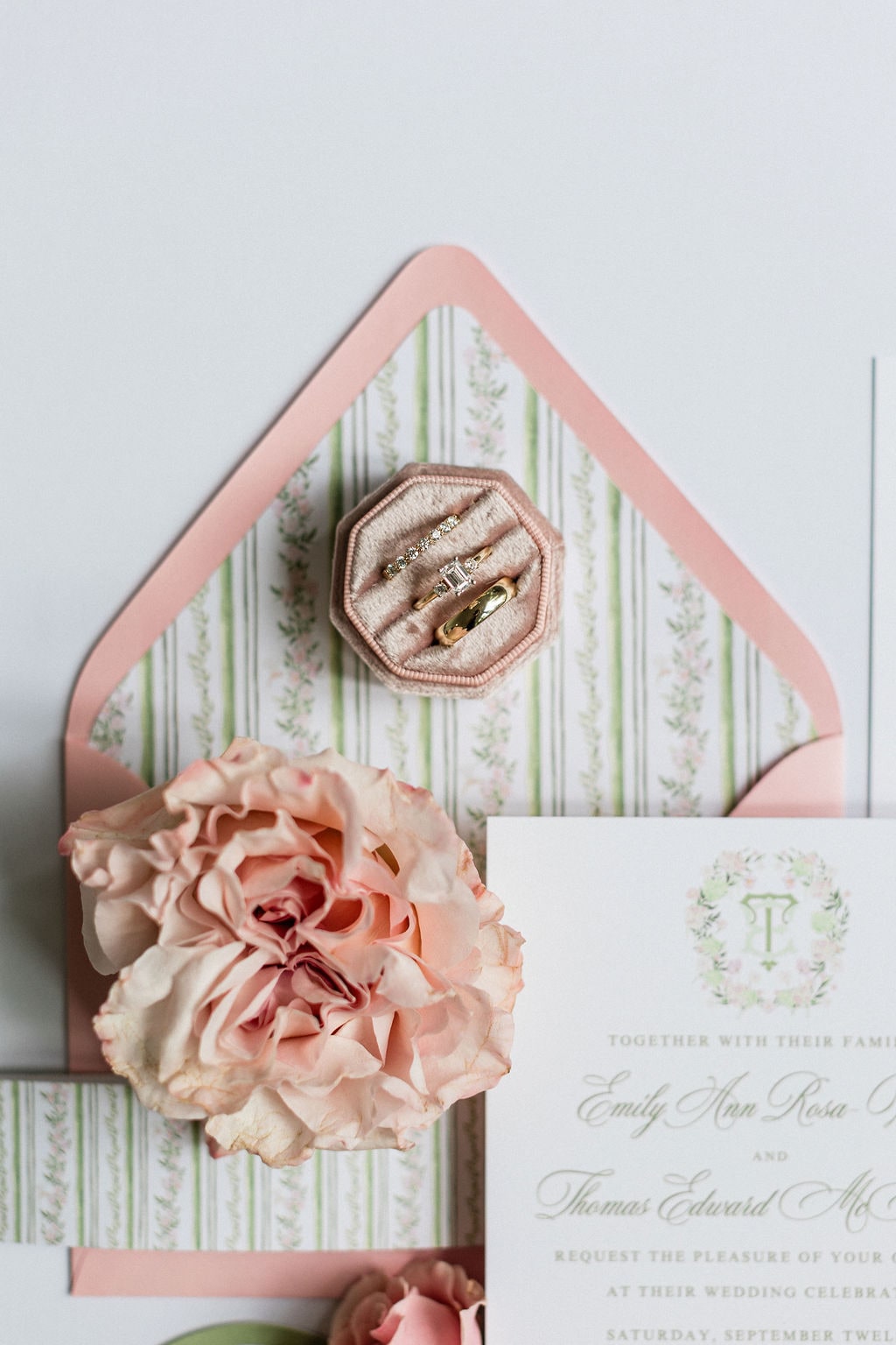 A blush garden rose beside the velvet ring box and the monogrammed invitation, on a green-and-pink striped envelope liner — from the Emily & Thomas wedding at Black Horse Manor