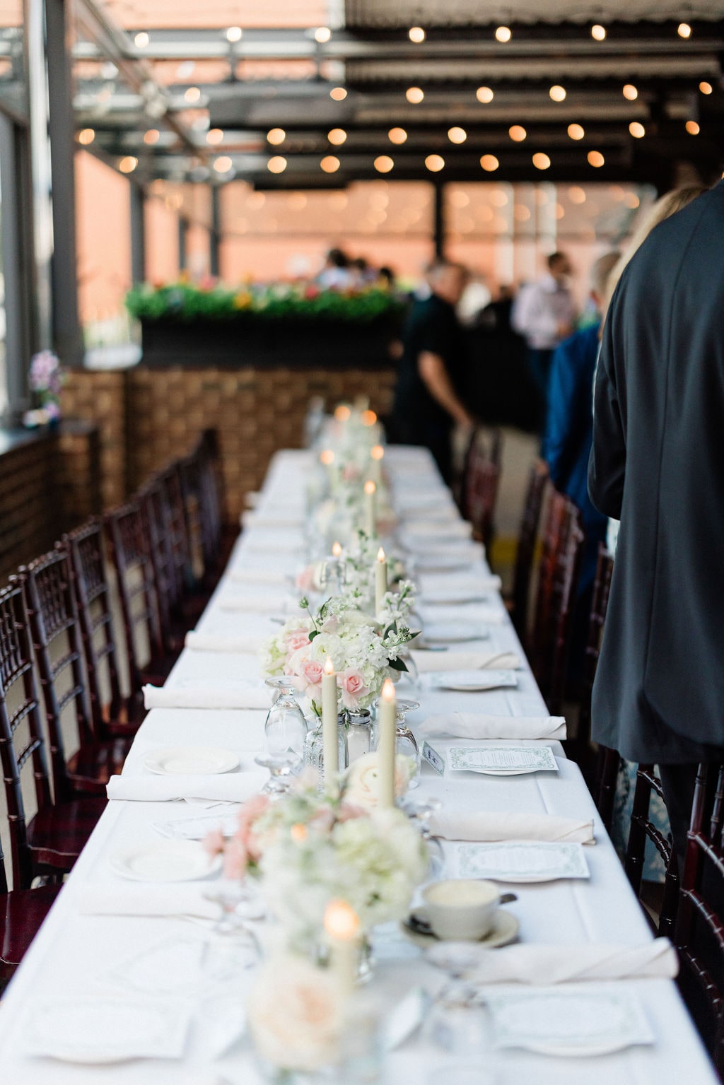 A long table under string lights with bud-vase centerpieces and tapers down its length at the Emily & Thomas wedding — designed by Lael Florals