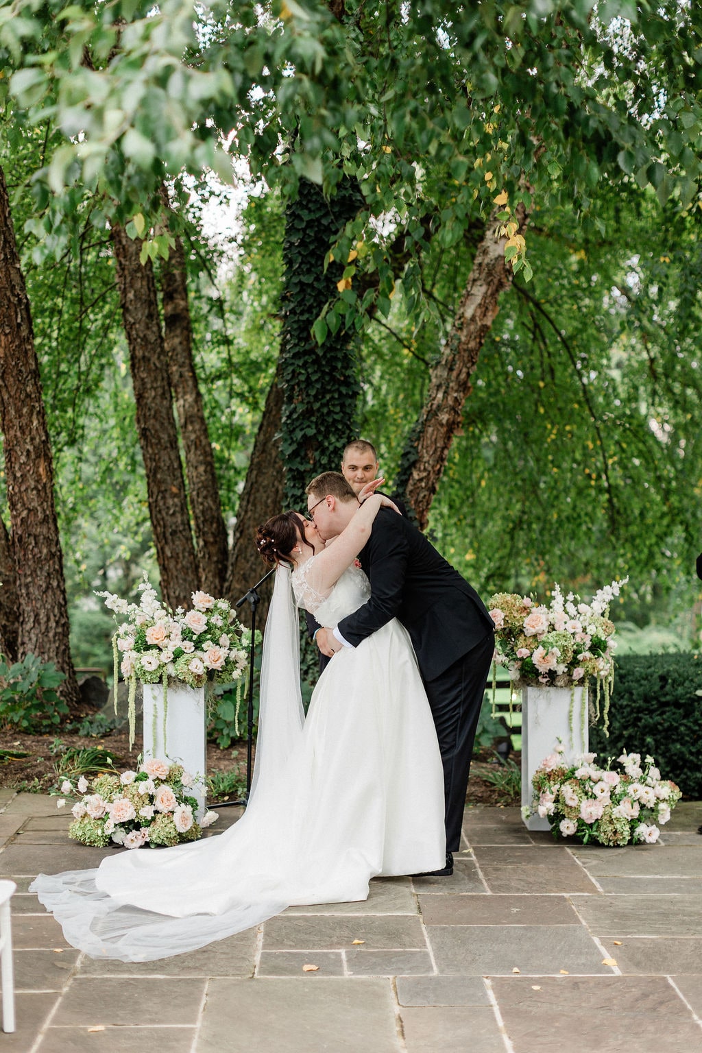 The kiss at the altar between the two pedestal arrangements at the Emily & Thomas wedding — designed by Lael Florals