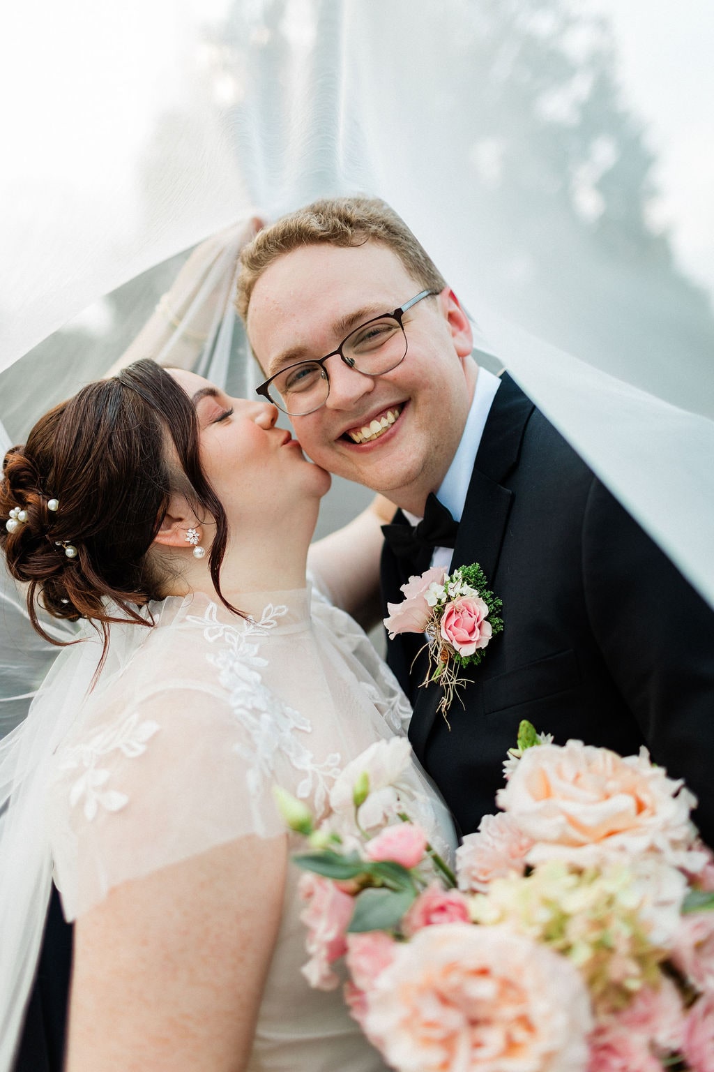 Under the veil, the bridal bouquet and the groom's pink boutonniere both in frame at the Emily & Thomas wedding — designed by Lael Florals