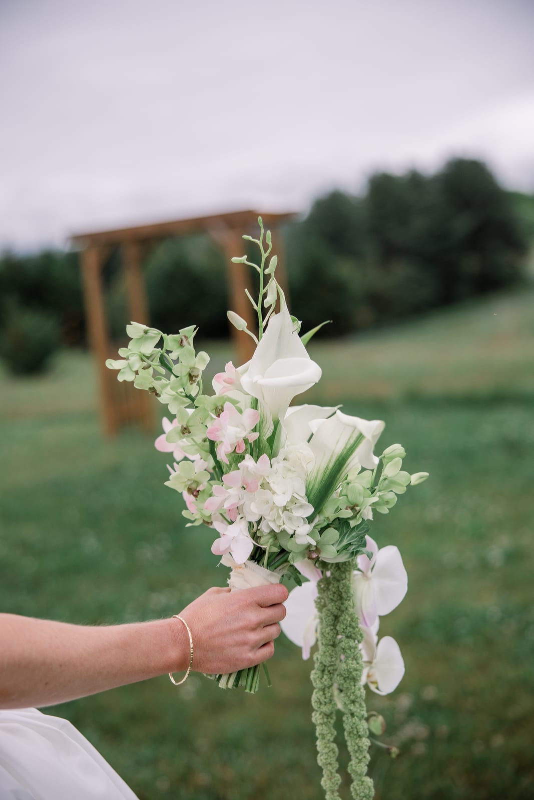 Bride's hand holding the cascade bouquet before the ceremony arbor at the Gabby & Matt wedding — designed by Lael Florals