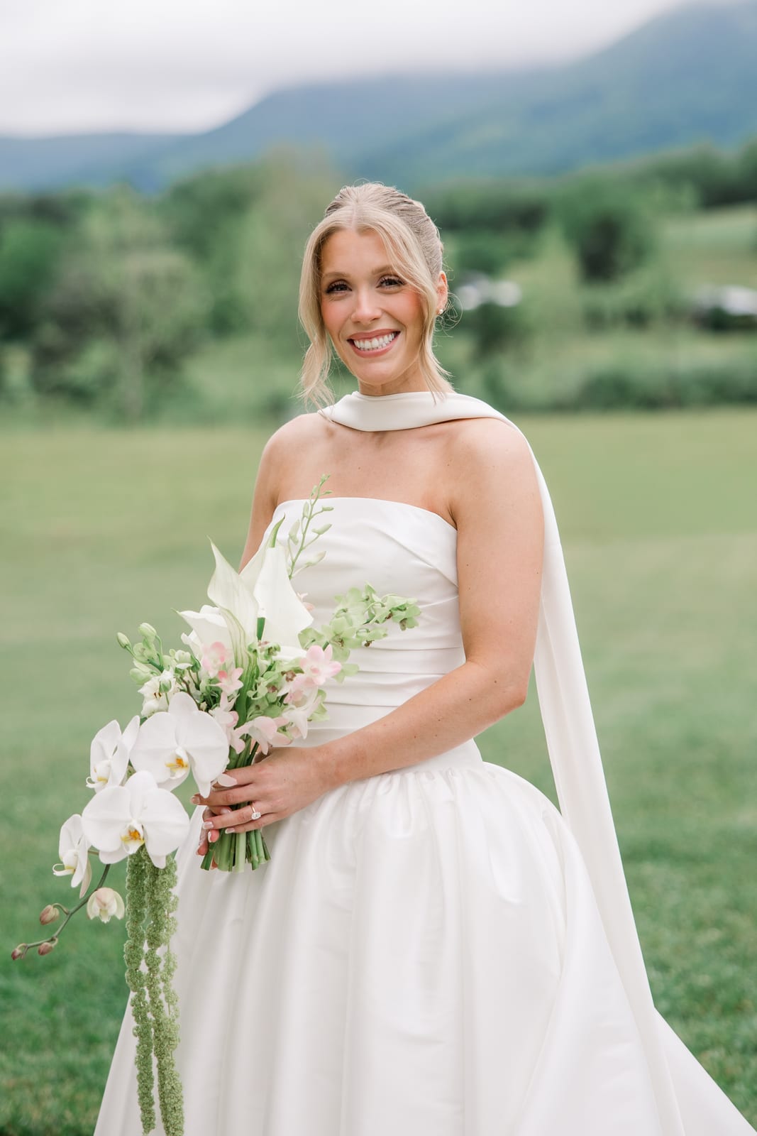 Bride holding a cascading orchid bouquet against mountains at the Gabby & Matt wedding — designed by Lael Florals
