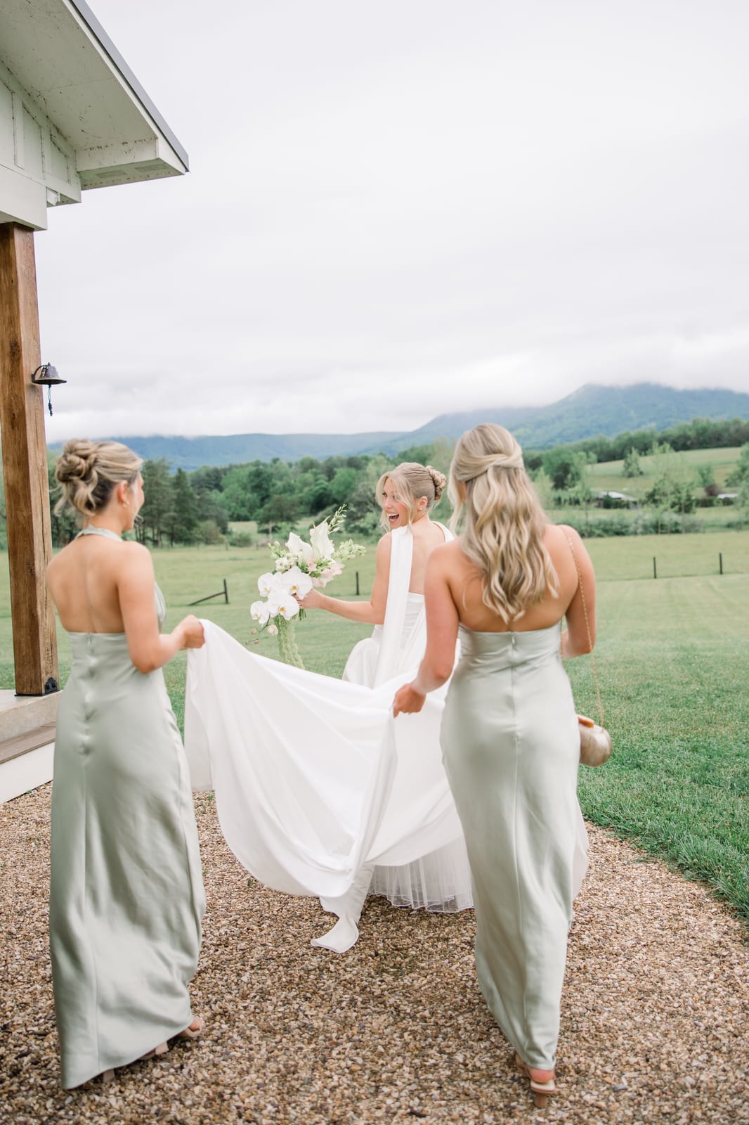 Bride carrying her white cascade bouquet as bridesmaids lift her train at the Gabby & Matt wedding — designed by Lael Florals