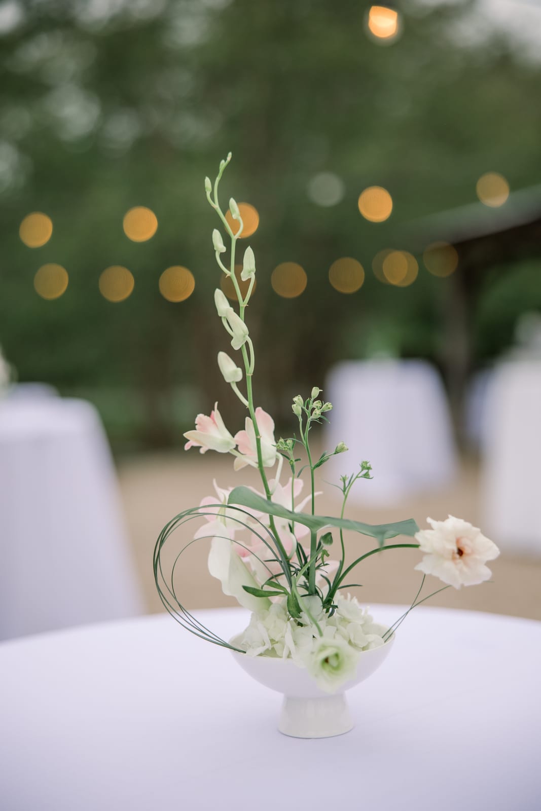 Sculptural orchid cocktail hour arrangement under string lights at the Gabby & Matt wedding — designed by Lael Florals