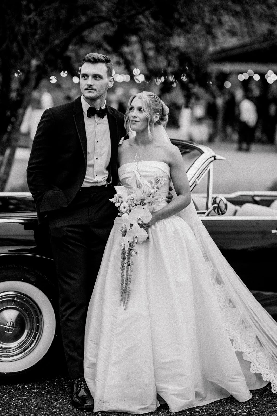 Bride and groom beside a vintage convertible with a cascading orchid bouquet at the Gabby & Matt wedding — designed by Lael Florals