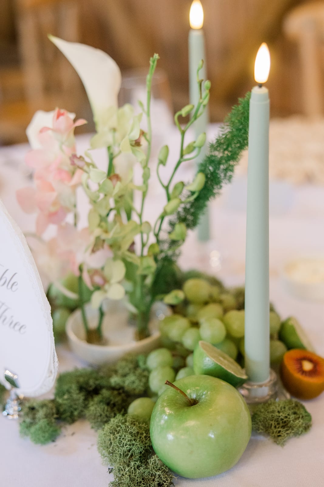 Fruit-styled centerpiece with green apple, grapes, lime, and white orchids at the Gabby & Matt wedding — designed by Lael Florals