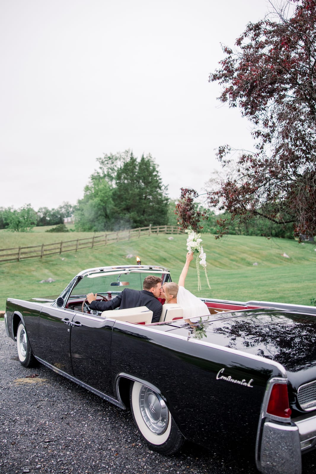 Bride raising her cascading orchid bouquet from the getaway car at the Gabby & Matt wedding — designed by Lael Florals