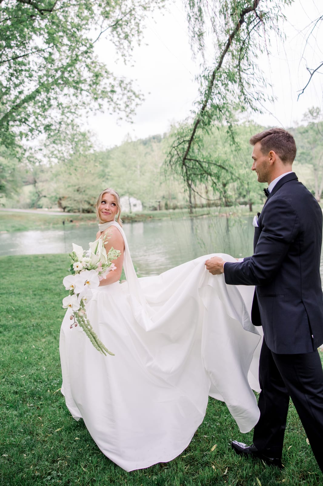 Groom carrying the bride's train as she holds her orchid cascade bouquet at the Gabby & Matt wedding — designed by Lael Florals
