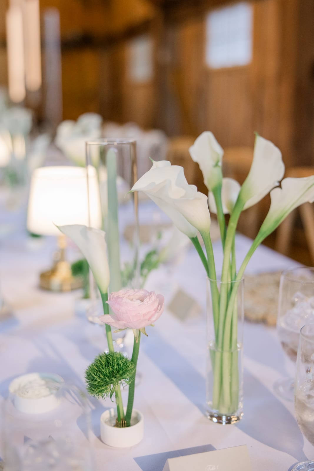 Calla lily bud vases and pink ranunculus down the head table at the Gabby & Matt wedding — designed by Lael Florals