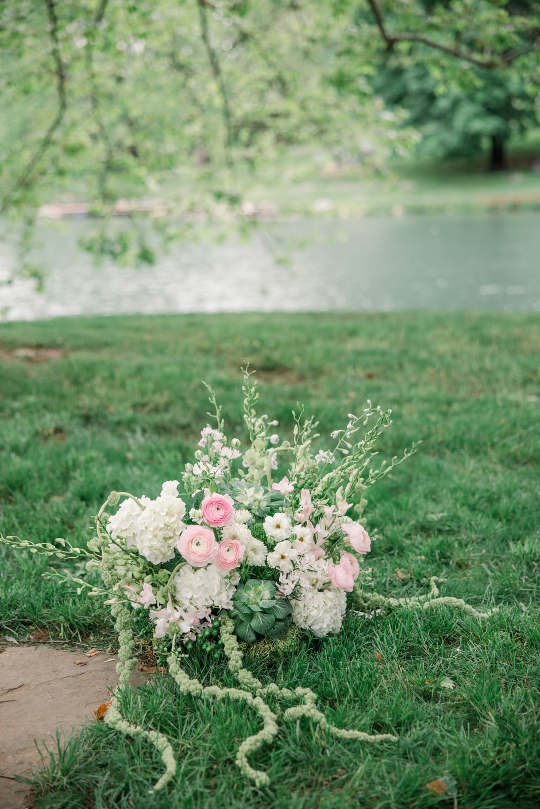 Pink ranunculus and hydrangea aisle arrangement by the lake at the Gabby & Matt wedding — designed by Lael Florals
