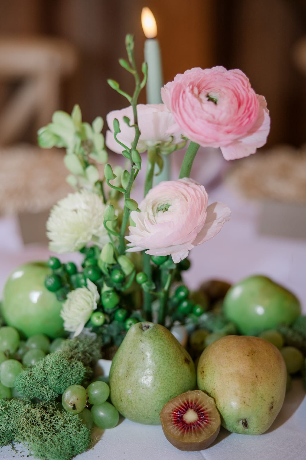 Pink ranunculus rising over pears and red kiwi in a fruit-styled centerpiece at the Gabby & Matt wedding — designed by Lael Florals