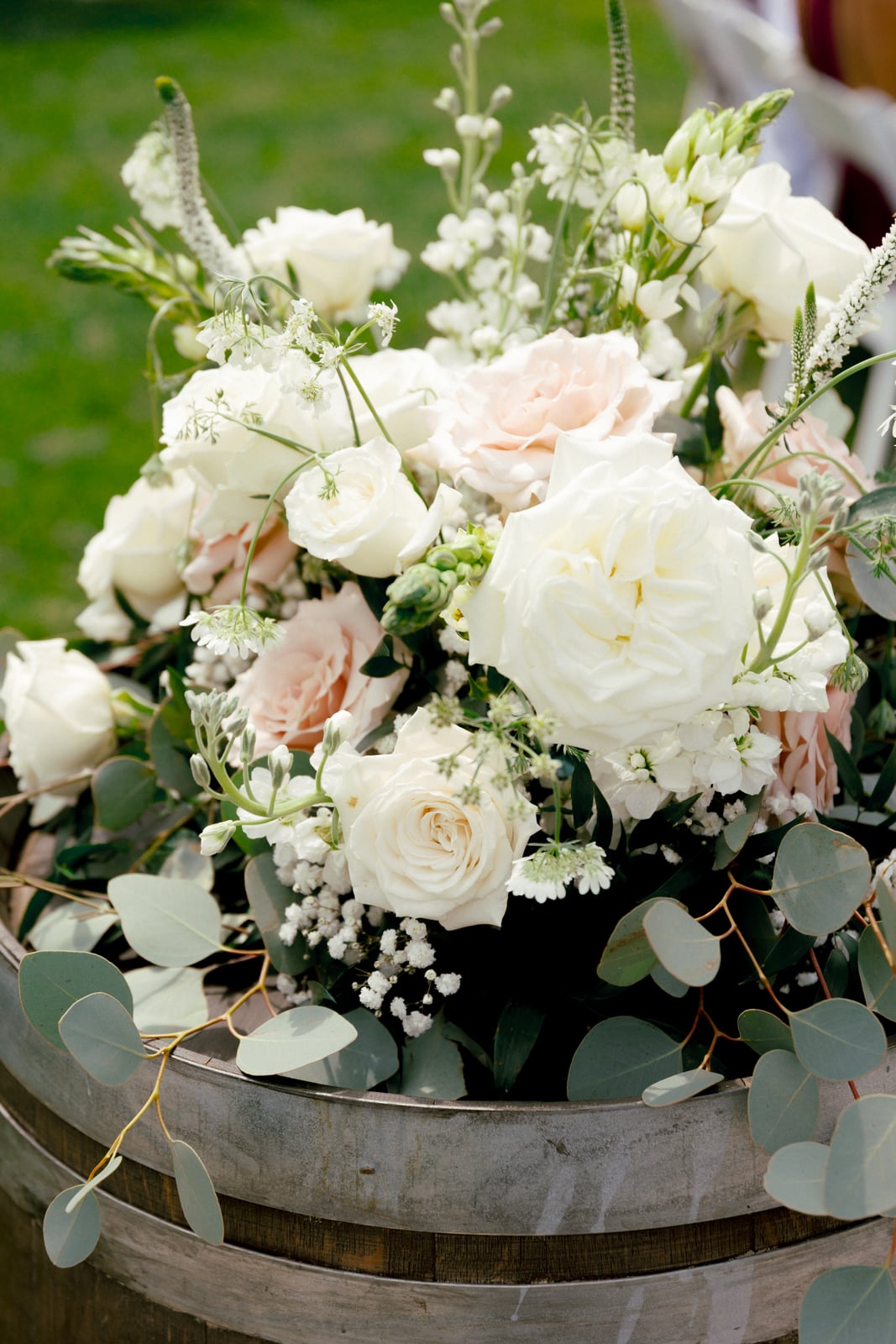 A loose garden-style arrangement of white and blush blooms with eucalyptus spilling over a barrel — designed by Lael Florals