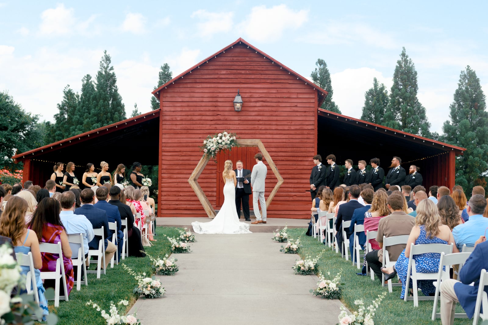 A barn wedding ceremony with garden-style florals on the arch and down the aisle — designed by Lael Florals