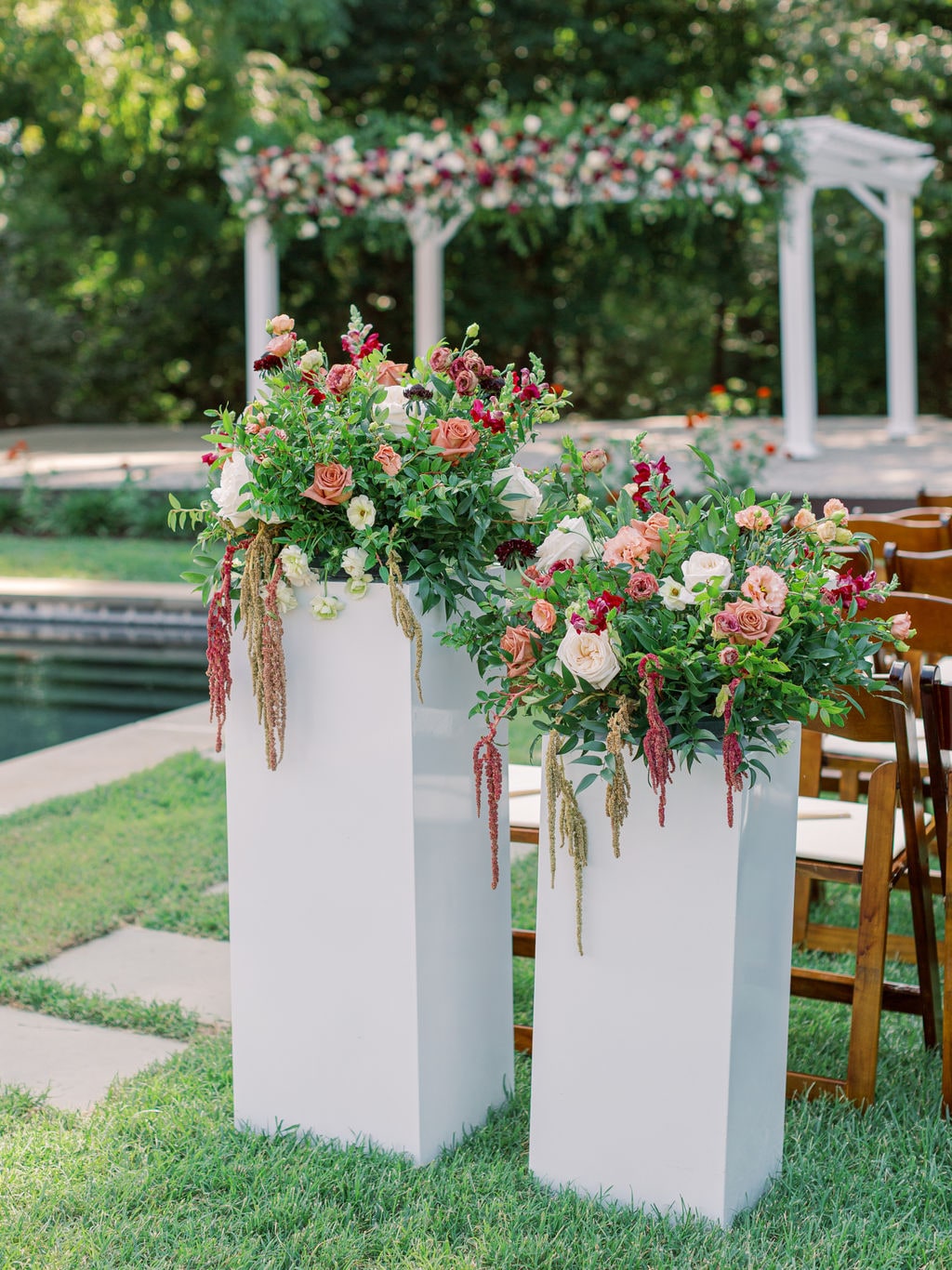 A pair of aisle pedestal arrangements with the flowered pergola behind at the Karlie & Hank wedding — designed by Lael Florals