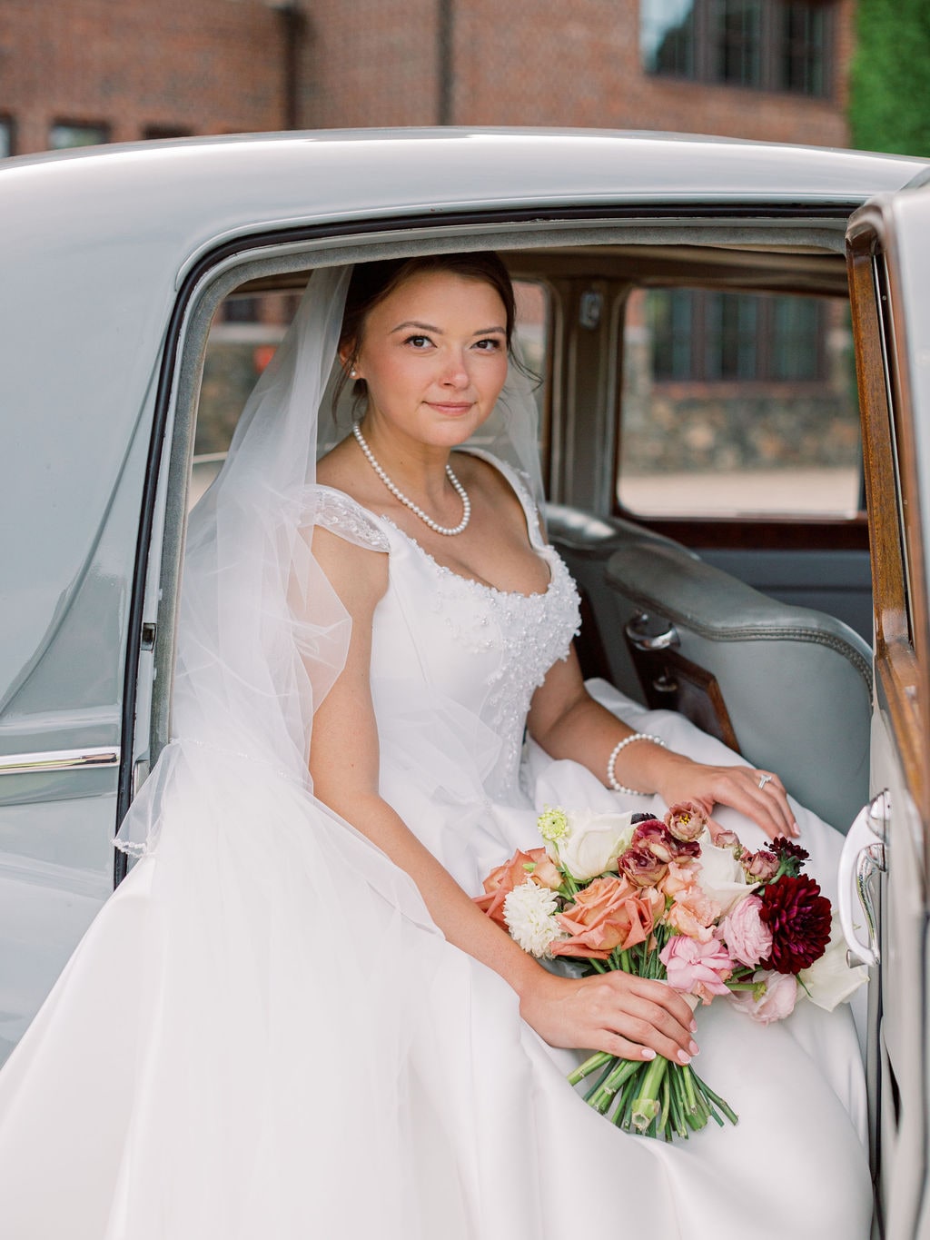 The bridal bouquet across her lap in the vintage car at the Karlie & Hank wedding — designed by Lael Florals