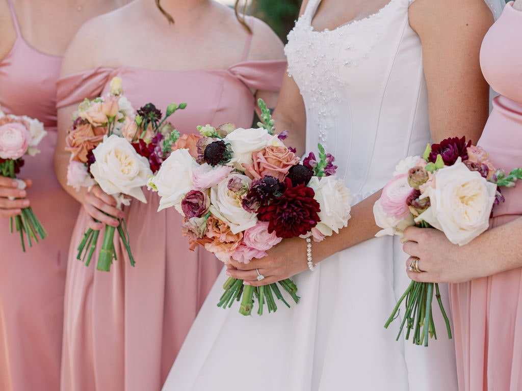 The bridal bouquet beside two bridesmaid bouquets in the same terracotta and burgundy palette at the Karlie & Hank wedding — designed by Lael Florals