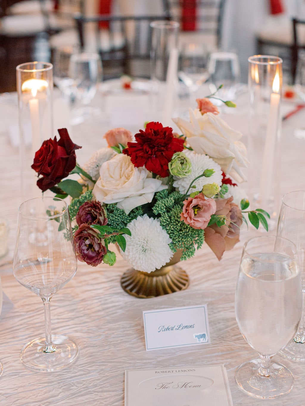 A gold compote centerpiece of burgundy dahlia, white ranunculus and blush garden roses at the Karlie & Hank wedding — designed by Lael Florals