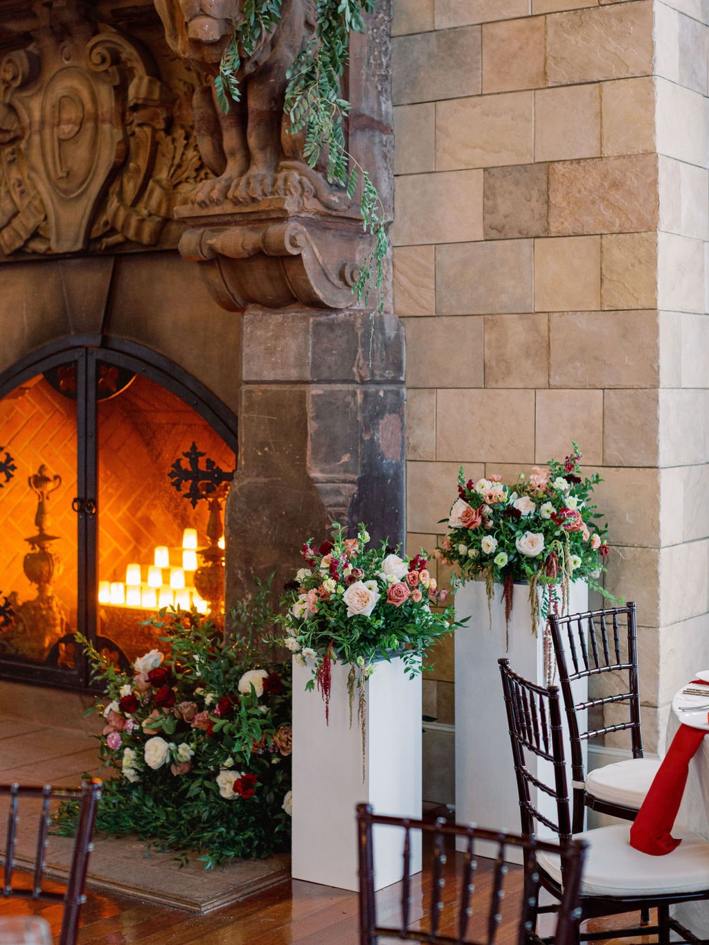 Pedestal arrangements flanking the carved stone fireplace at the Karlie & Hank wedding — designed by Lael Florals