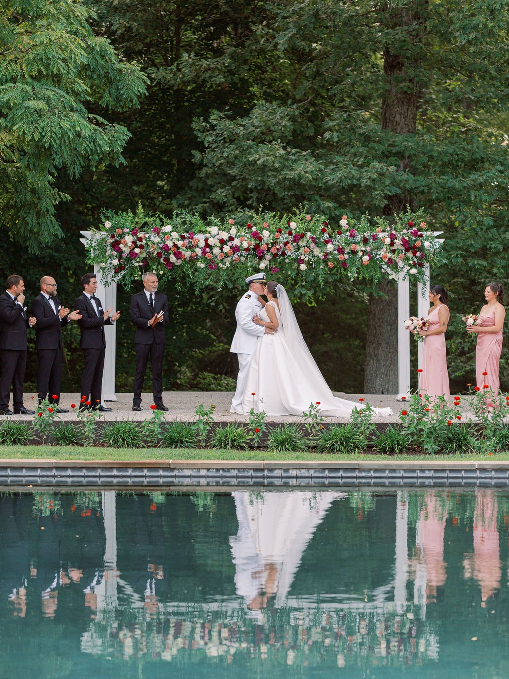 The flowered ceremony arch mirrored in the reflecting pool at the Karlie & Hank wedding — designed by Lael Florals