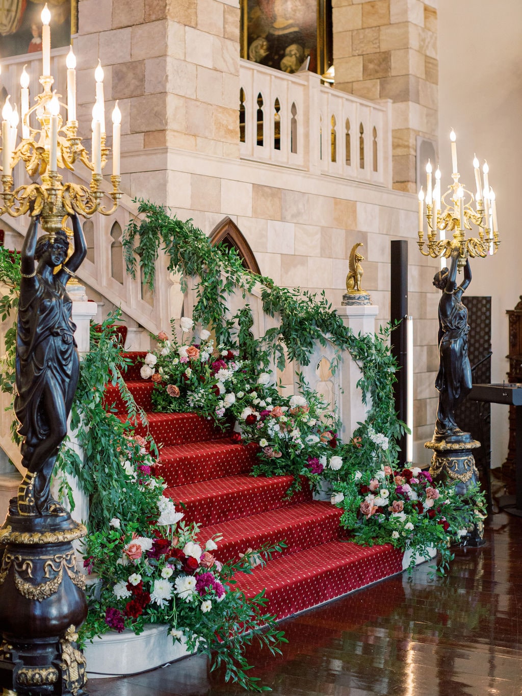 Greenery and blooms garlanding the great staircase up toward the chandeliers at the Karlie & Hank wedding — designed by Lael Florals