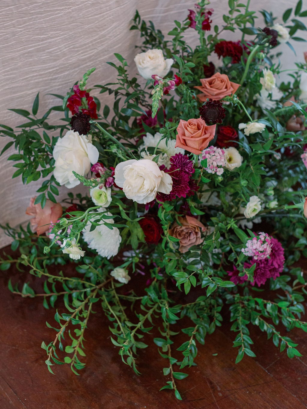 A ground arrangement of garden roses, burgundy dahlias and trailing greenery at the Karlie & Hank wedding — designed by Lael Florals