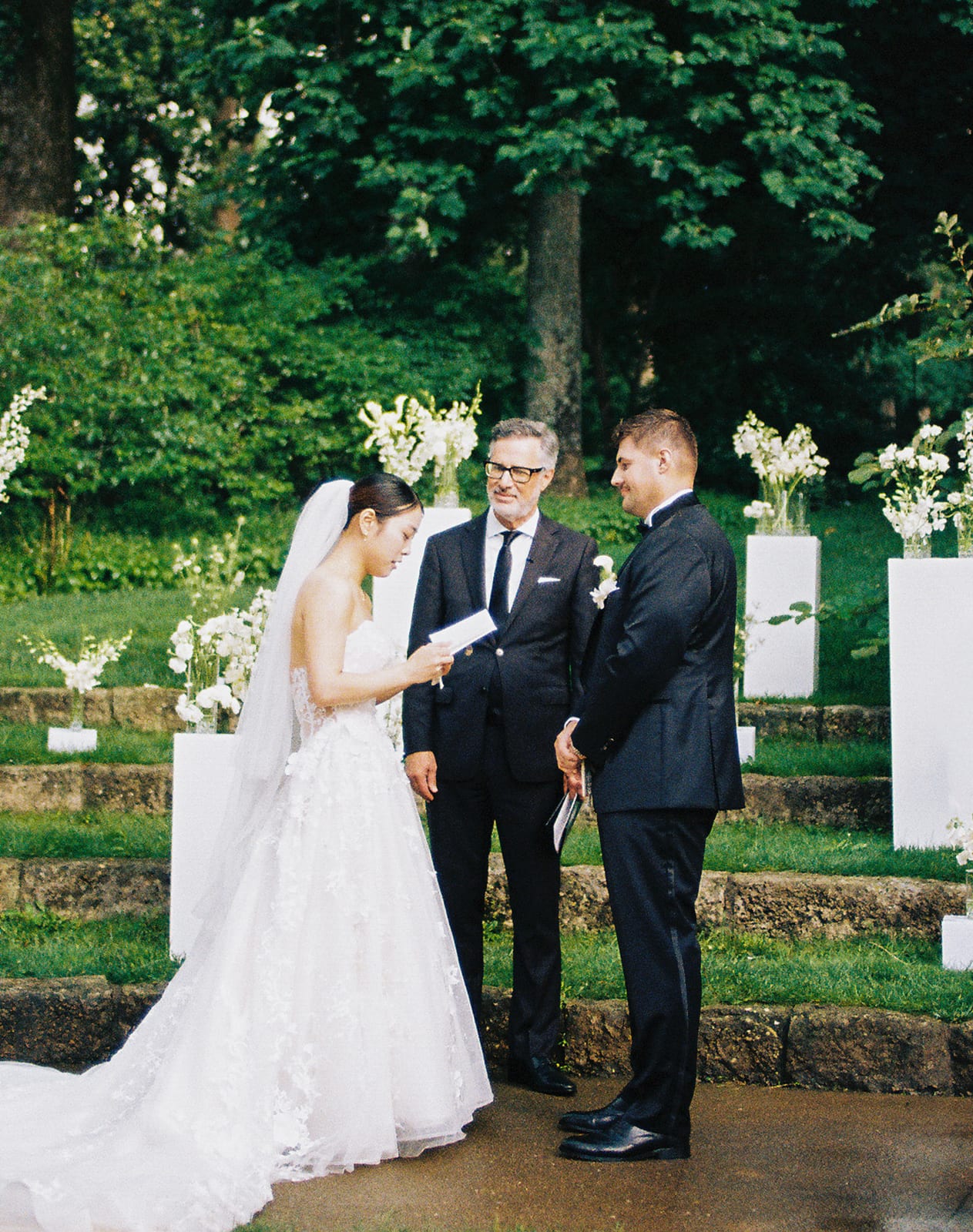 Bride reading her vows framed by white pedestal florals at the Sharon & Matt wedding — designed by Lael Florals