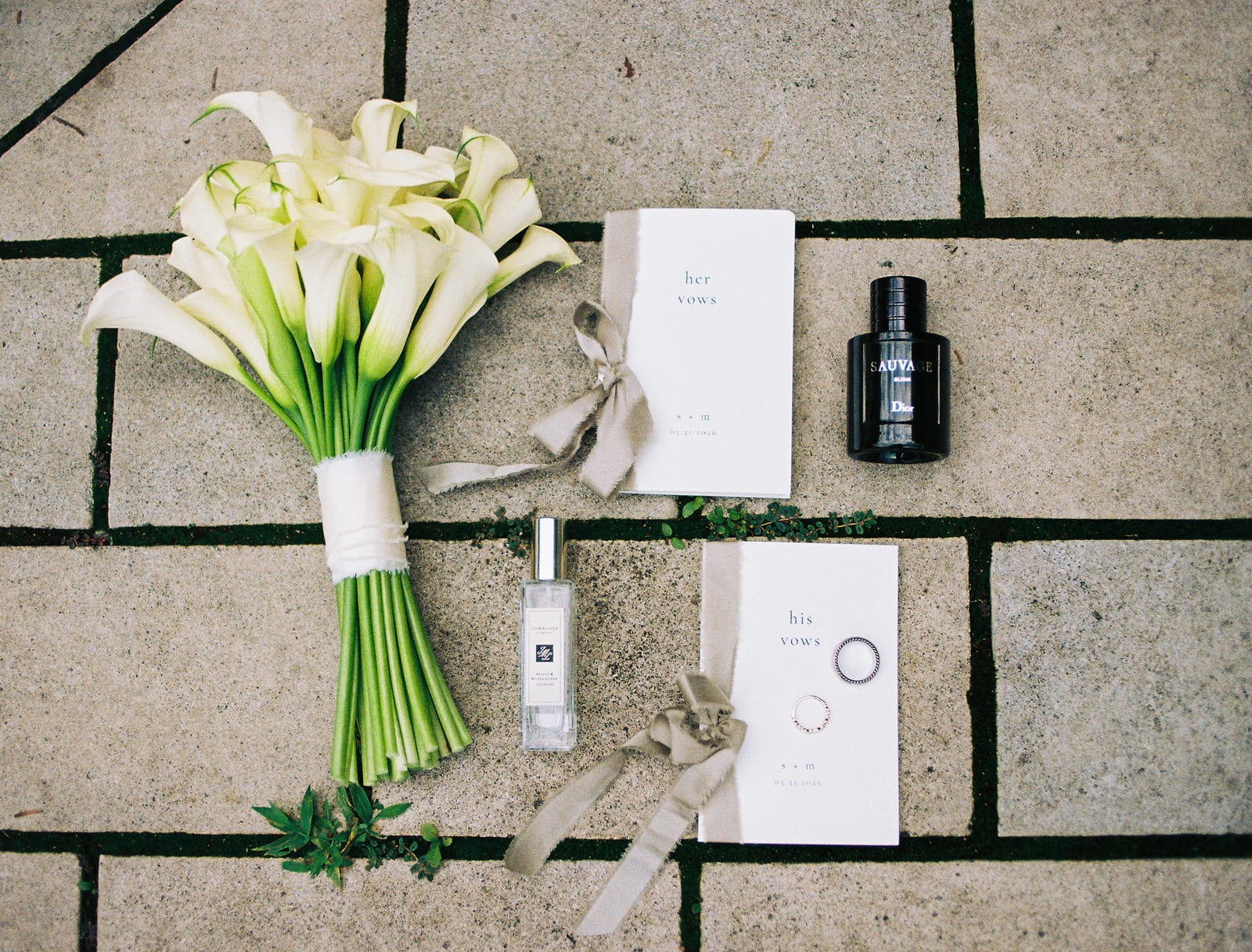 The bridal bouquet of white calla lilies tied with ribbon, laid on stone beside vow books and perfume — styled flat lay from a Nashville wedding by Lael Florals