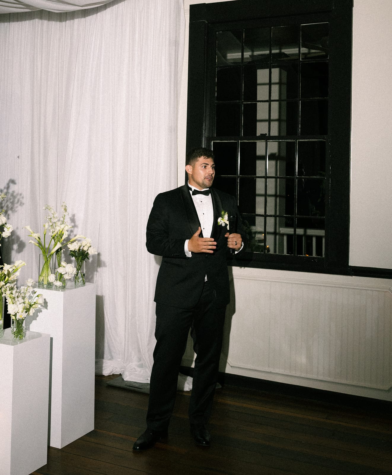 Groom giving a toast beside white bud vase pedestals at the Sharon & Matt wedding — designed by Lael Florals
