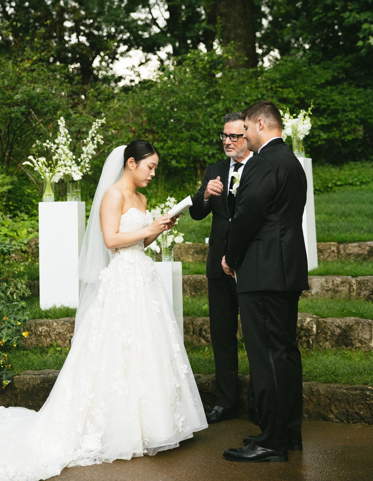 Bride reading vows beside calla and delphinium pedestal arrangements at the Sharon & Matt wedding — designed by Lael Florals