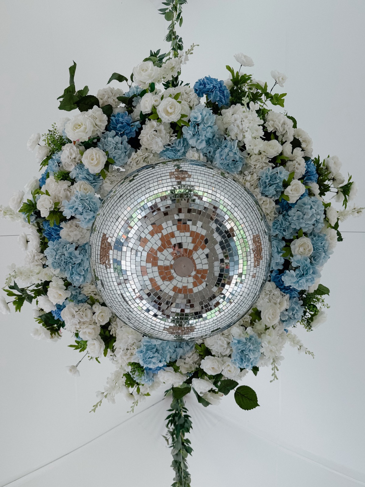 Looking up at the suspended chandelier: the mirror ball ringed by blue hydrangea and white roses, greenery trailing off its edges