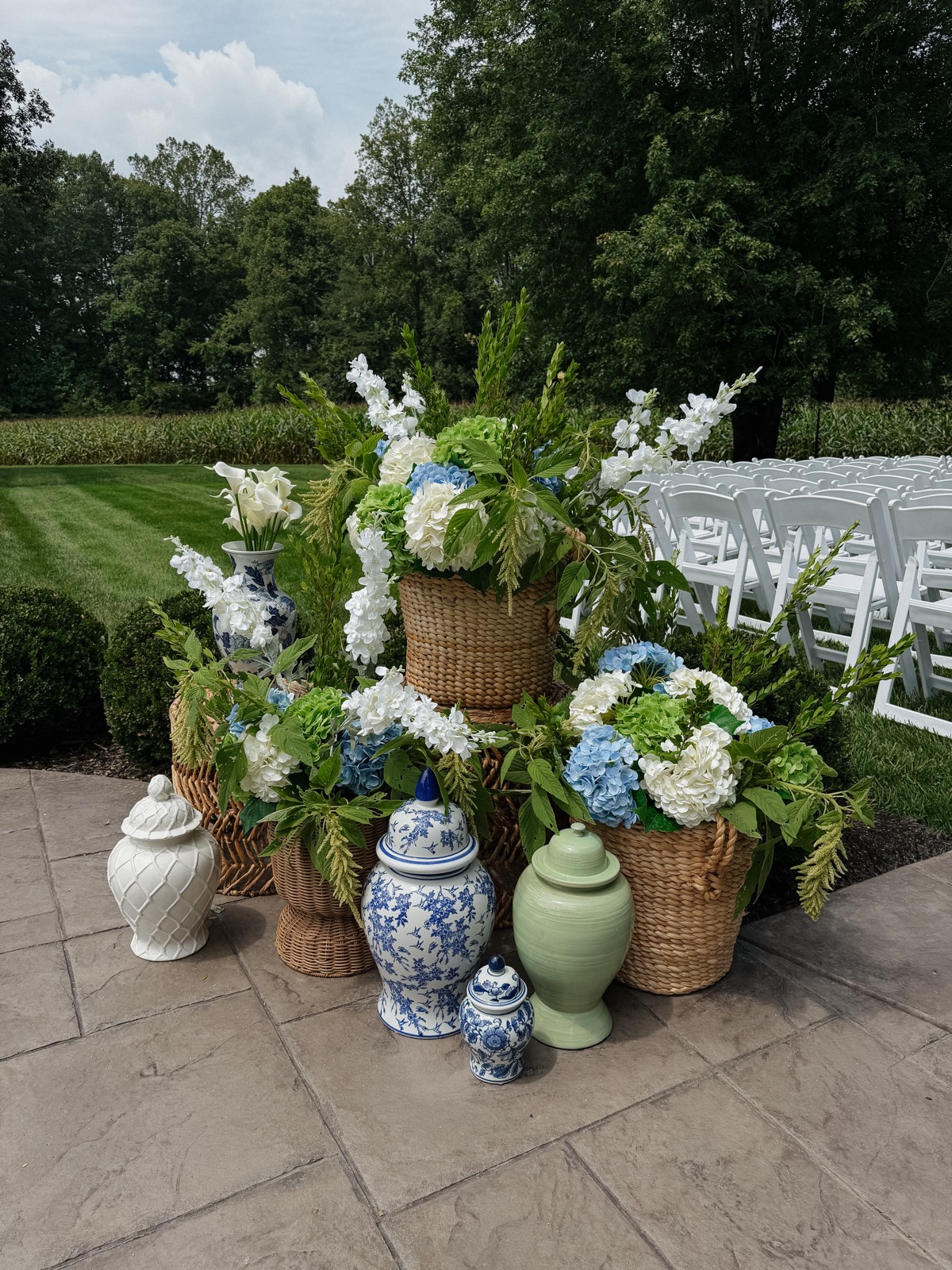 Woven baskets and ginger jars at the ceremony entrance filled with blue, green, and white hydrangea and cascades of trailing amaranth