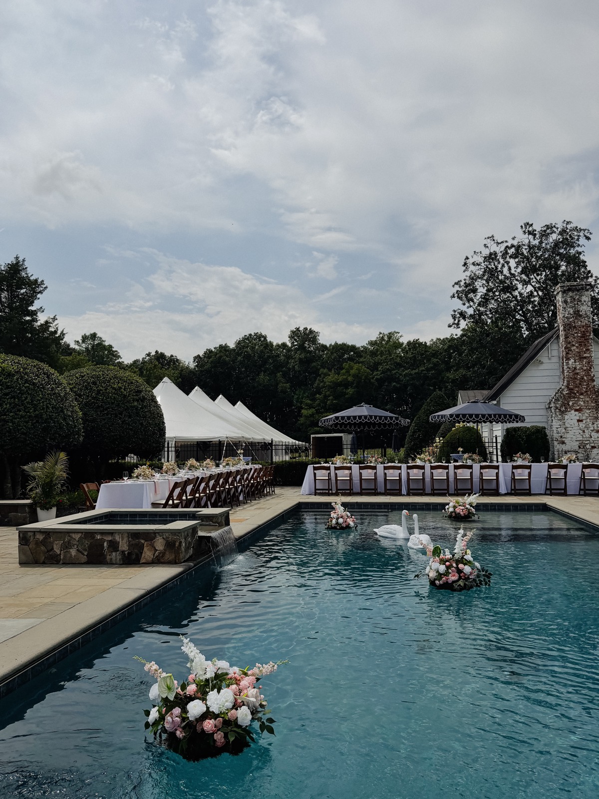 The pool at Historic Whitewood ringed by dinner tables, with the estate's white clapboard cottage and the sailcloth tent peaks beyond